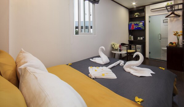 A hotel room with a bed, pillows, a TV, a small table with a vase, and a shower area. - Mayflower Hotel Hanoi (Hanoi)