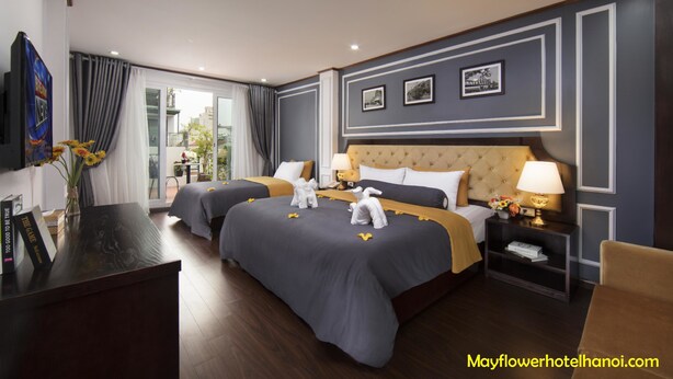 Quarto de hotel com duas camas, televisão, secretária e varanda com cortinas.