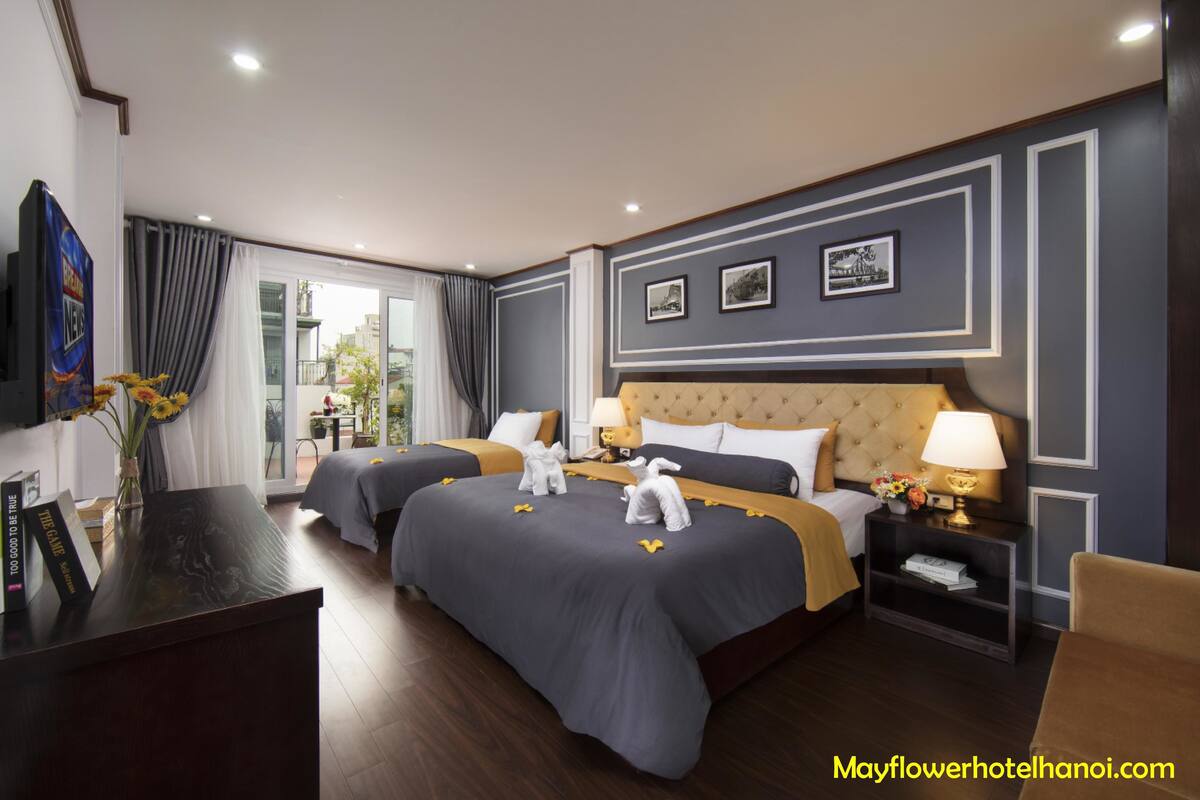 Habitación de hotel con dos camas, televisión, escritorio y balcón con cortinas.