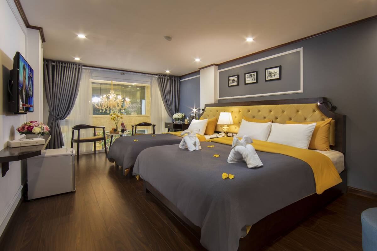 Habitación de hotel con dos camas, un escritorio, una silla, una araña y una ventana con cortinas.