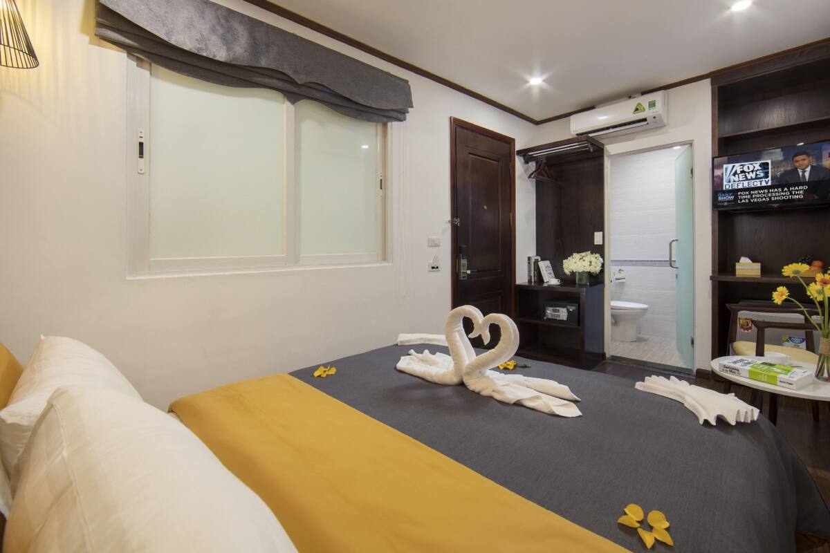 Una habitación de hotel con cama, televisión, baño y una pequeña mesa con flores.