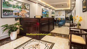 Uma área de recepção de hotel com balcão, quadros decorativos na parede, placa de recepção e planta em vaso.