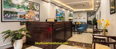 A hotel reception area with a reception desk, framed pictures on the wall, a reception sign, and a potted plant.