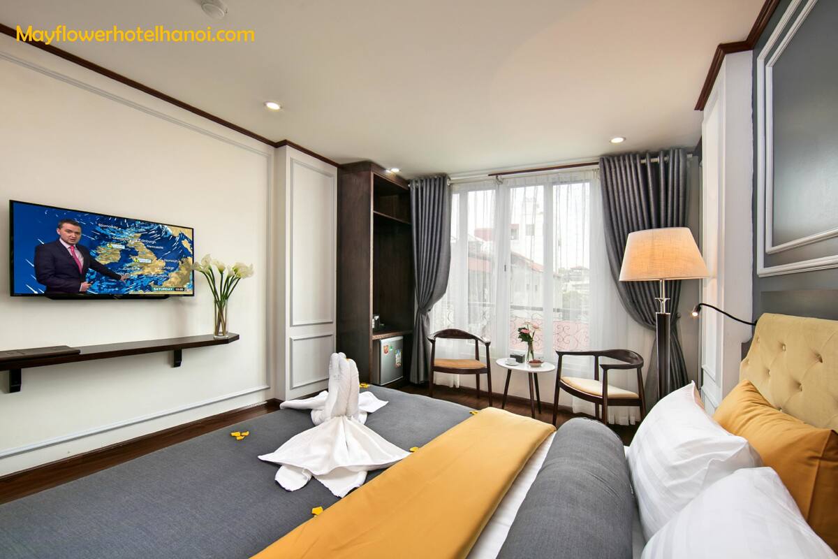 Una habitación de hotel con cama, escritorio, silla, televisor y ventana con cortinas.