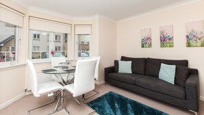 Un salon moderne avec une table à manger en verre, des chaises blanches, un canapé gris foncé et un tapis bleu.