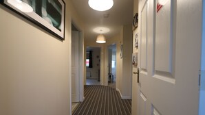 Un couloir avec un tapis à rayures, des murs blancs et un luminaire au plafond.