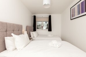 A hotel room with two beds, a large window with curtains, a headboard, and a framed picture on the wall.