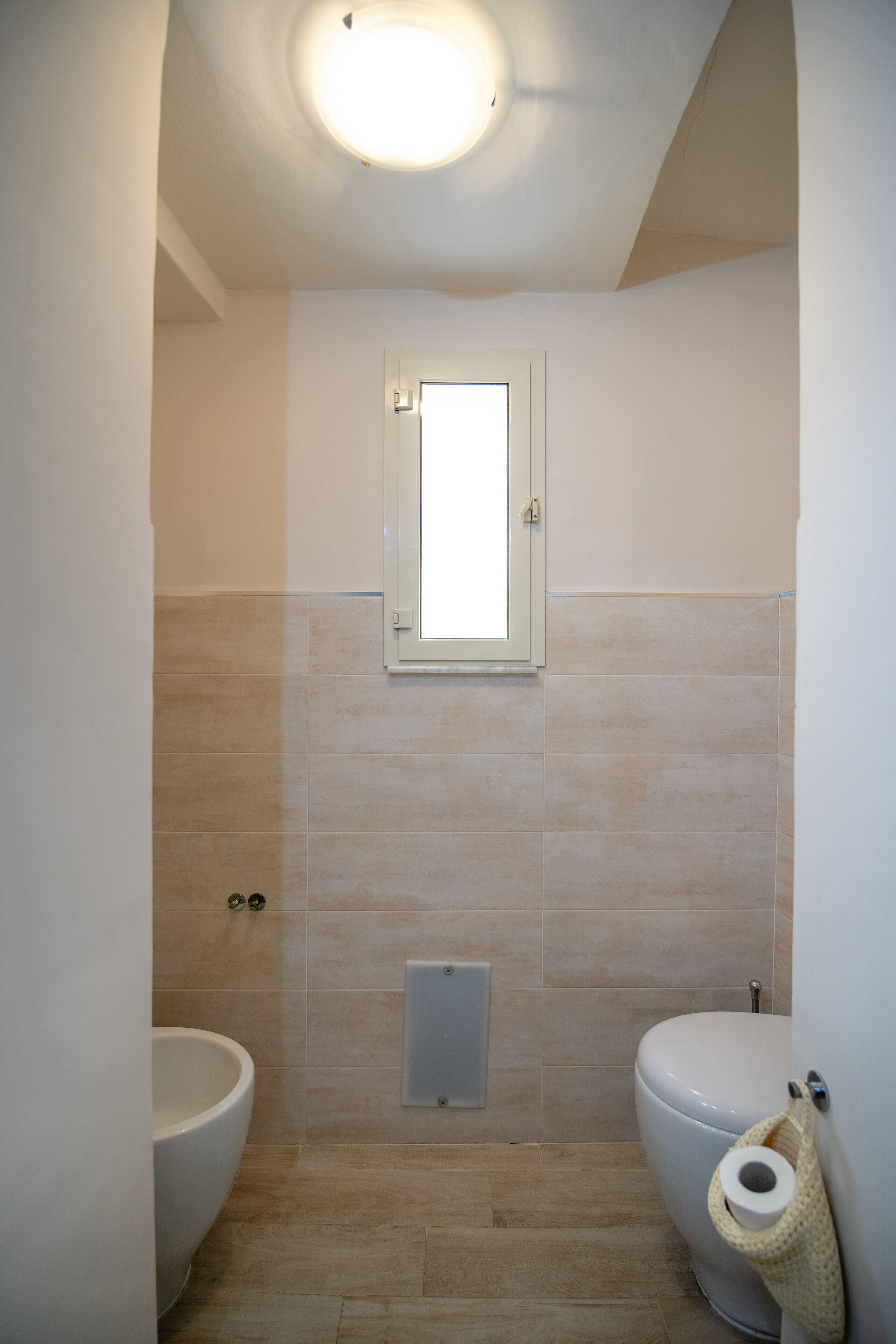 A bathroom with a toilet, bidet, and a small window.