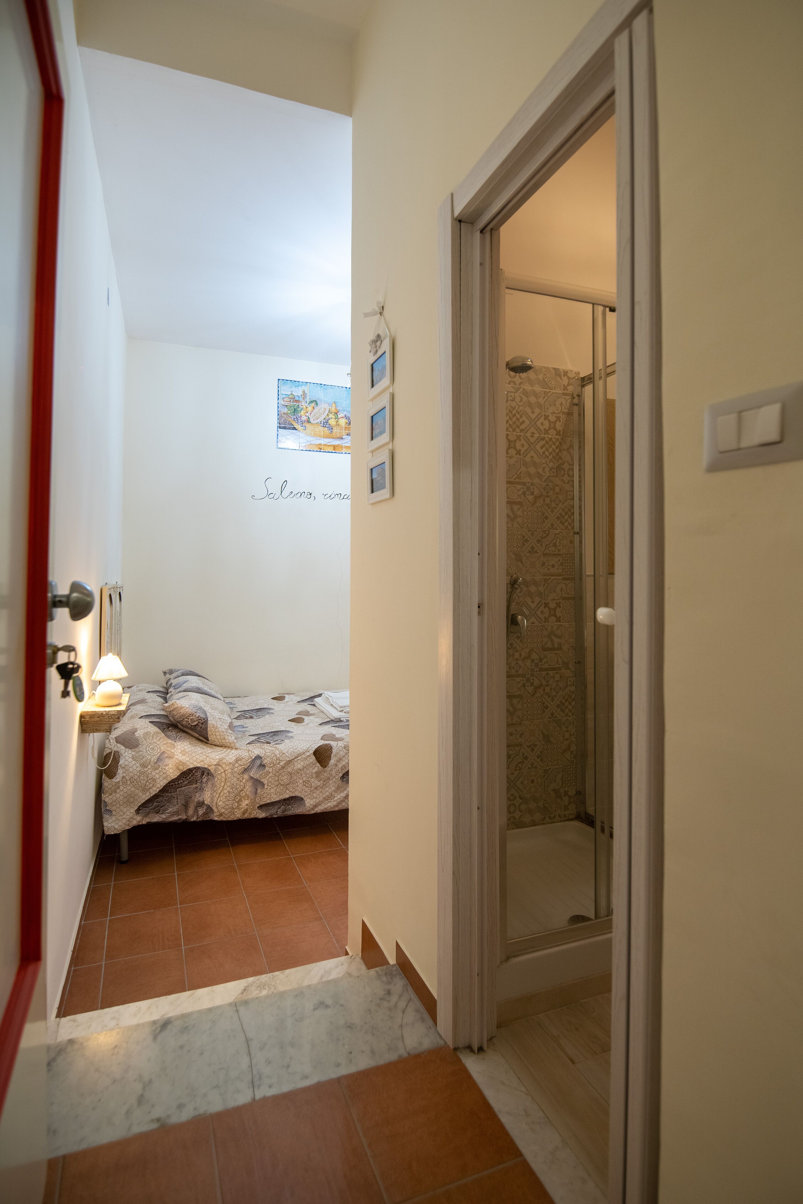 Un couloir étroit mène à une chambre à coucher qui contient un lit, une table de chevet avec une lampe et un espace douche.