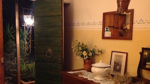 Una habitación con puerta de madera, una planta pequeña en maceta, una maceta blanca, un cuadro en marco y un espejo en la pared.
