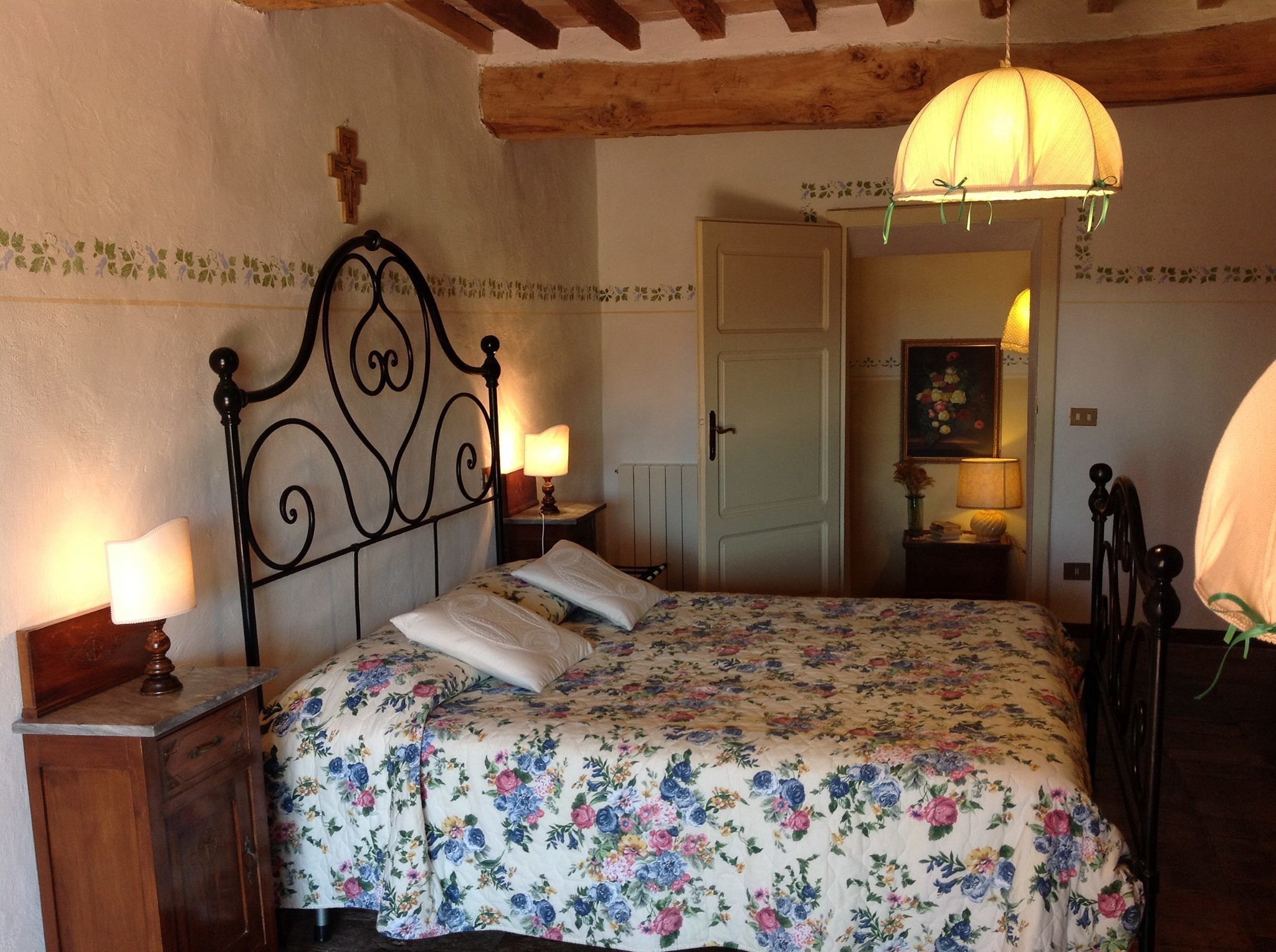 A bedroom with a floral bedspread, a wooden headboard, two bedside lamps, and a hanging light fixture.