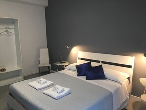 A modern hotel room with a neatly made bed, a bedside table with a lamp, and a chair. - Vatican Central Suites (Rome)