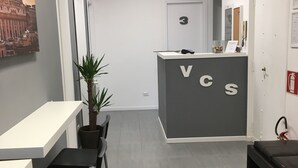 A reception desk with 'VCS' signage, a potted plant, and a chair. - Vatican Central Suites (Rome)