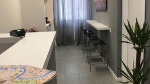 A modern office space with a reception desk, a large window with curtains, a painting on the wall, and a potted plant. - Vatican Central Suites (Rome)