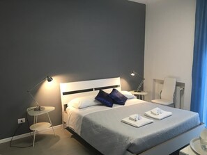 A modern hotel room with a large bed, two bedside tables, and a small round table. - Vatican Central Suites (Rome)