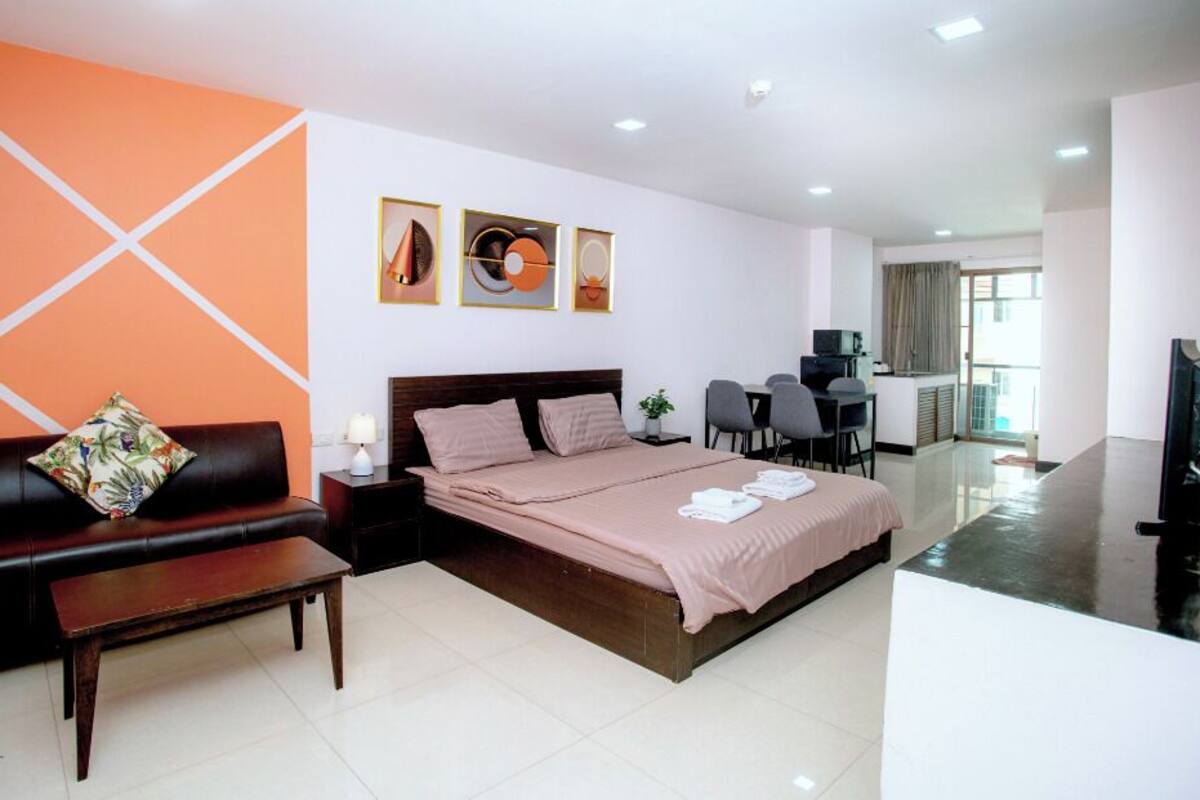 A modern hotel room with a bed, a sofa, a desk, and a TV.