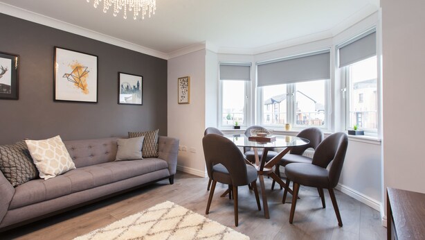 A modern living room with a grey sofa, a dining table with chairs, and a chandelier.