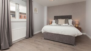 A bedroom with a large bed, two bedside lamps, a chandelier, a radiator, and a window with curtains.
