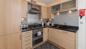 A modern kitchen with light wood cabinets, stainless steel appliances, and a black countertop.