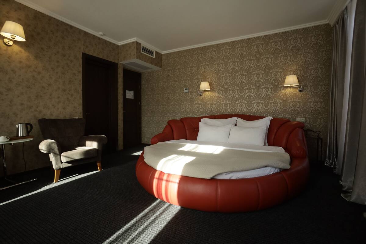 A hotel room with a large bed, a chair, a lamp, and a wall with a patterned design.