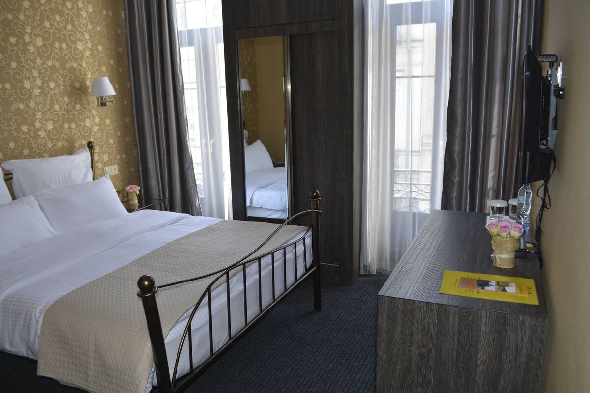 A hotel room with a bed, a desk, a mirror, and a window with curtains.