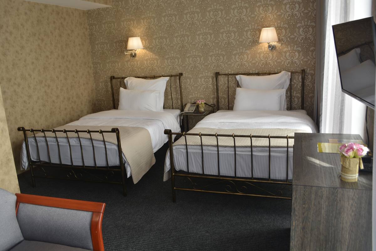 A hotel room with two single beds, a small desk with a telephone, and a television on the wall.