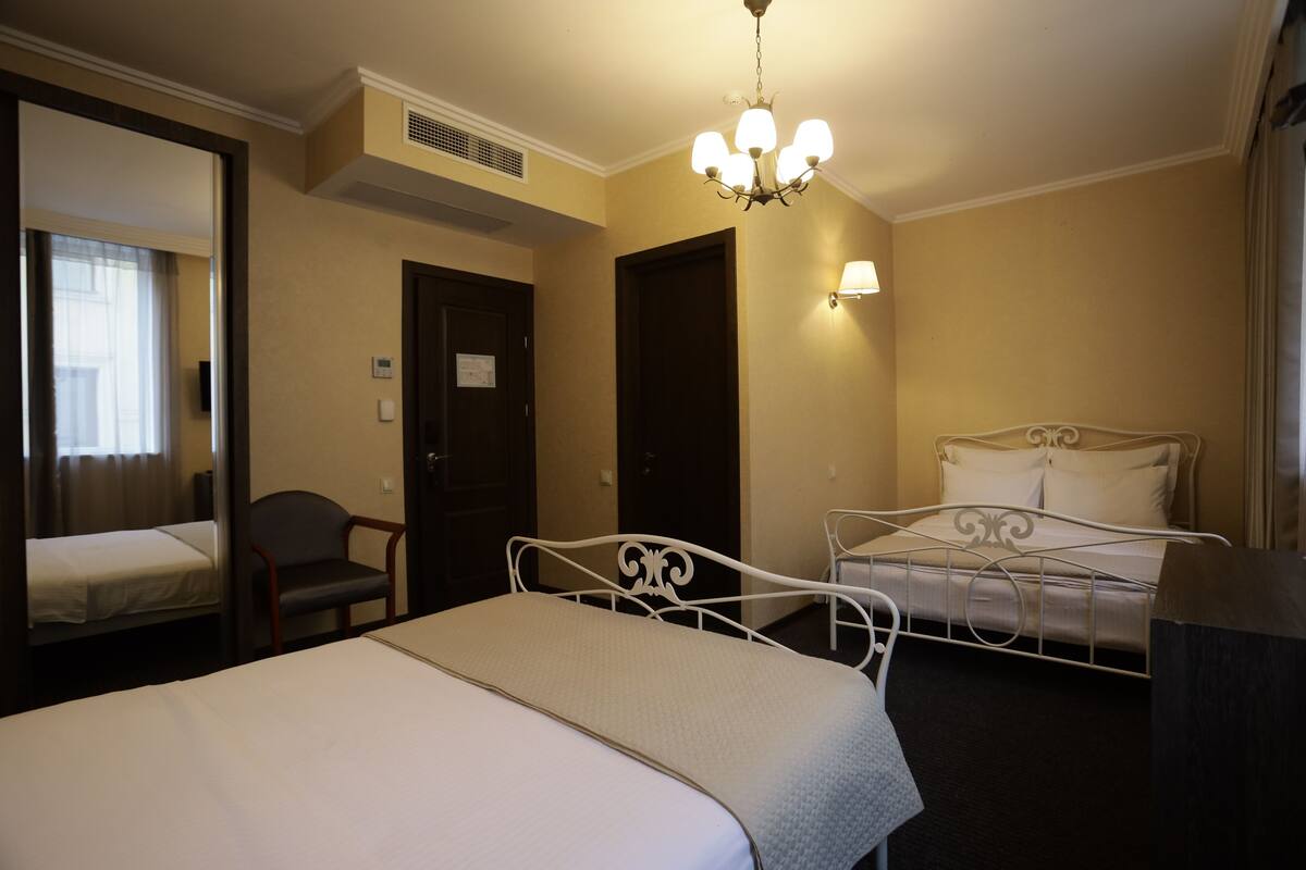A hotel room with a single bed, a chair, a desk, and a mirror.