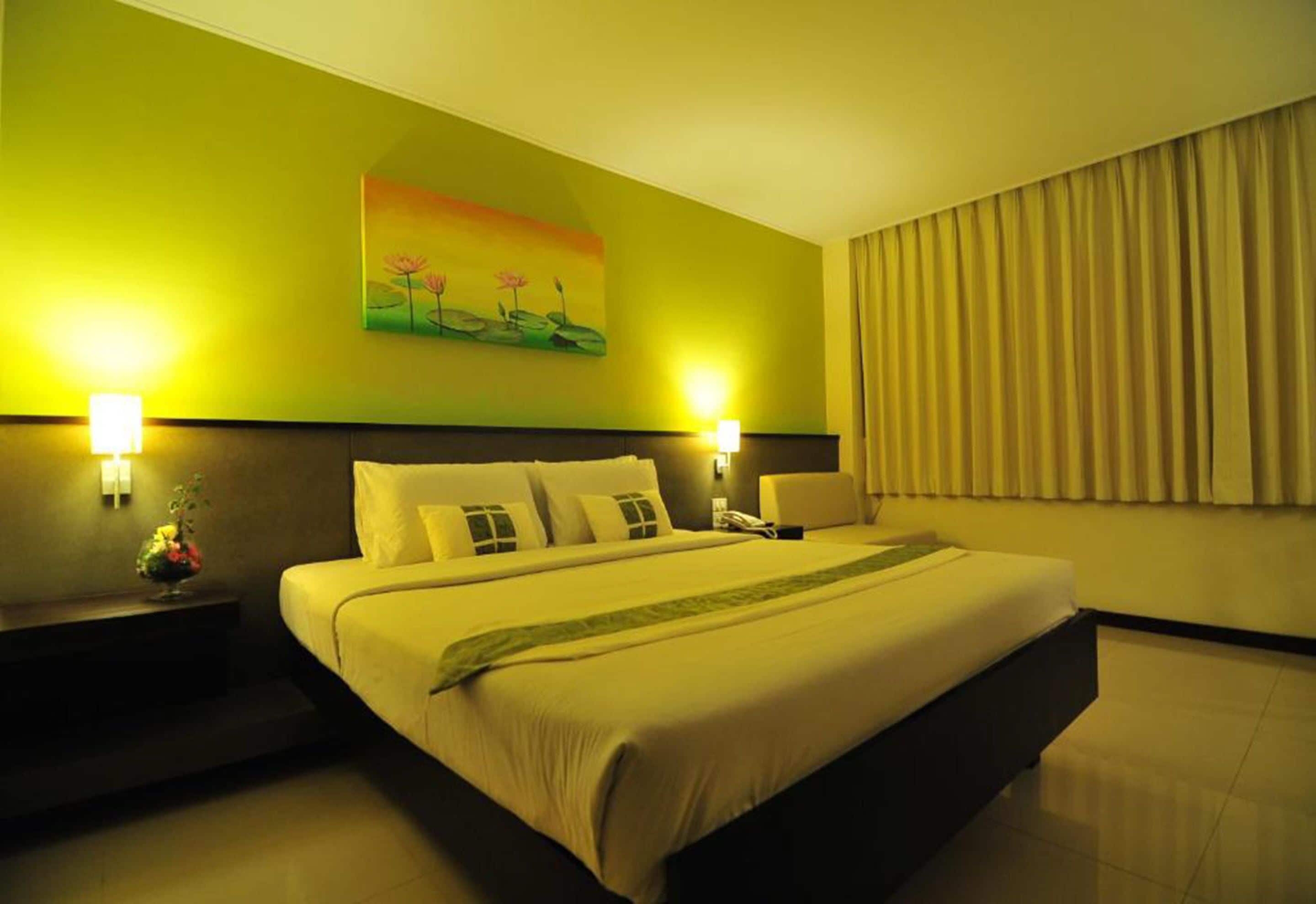 A hotel room with a large bed, two bedside tables with lamps, a painting on the wall, and a curtain on the window.