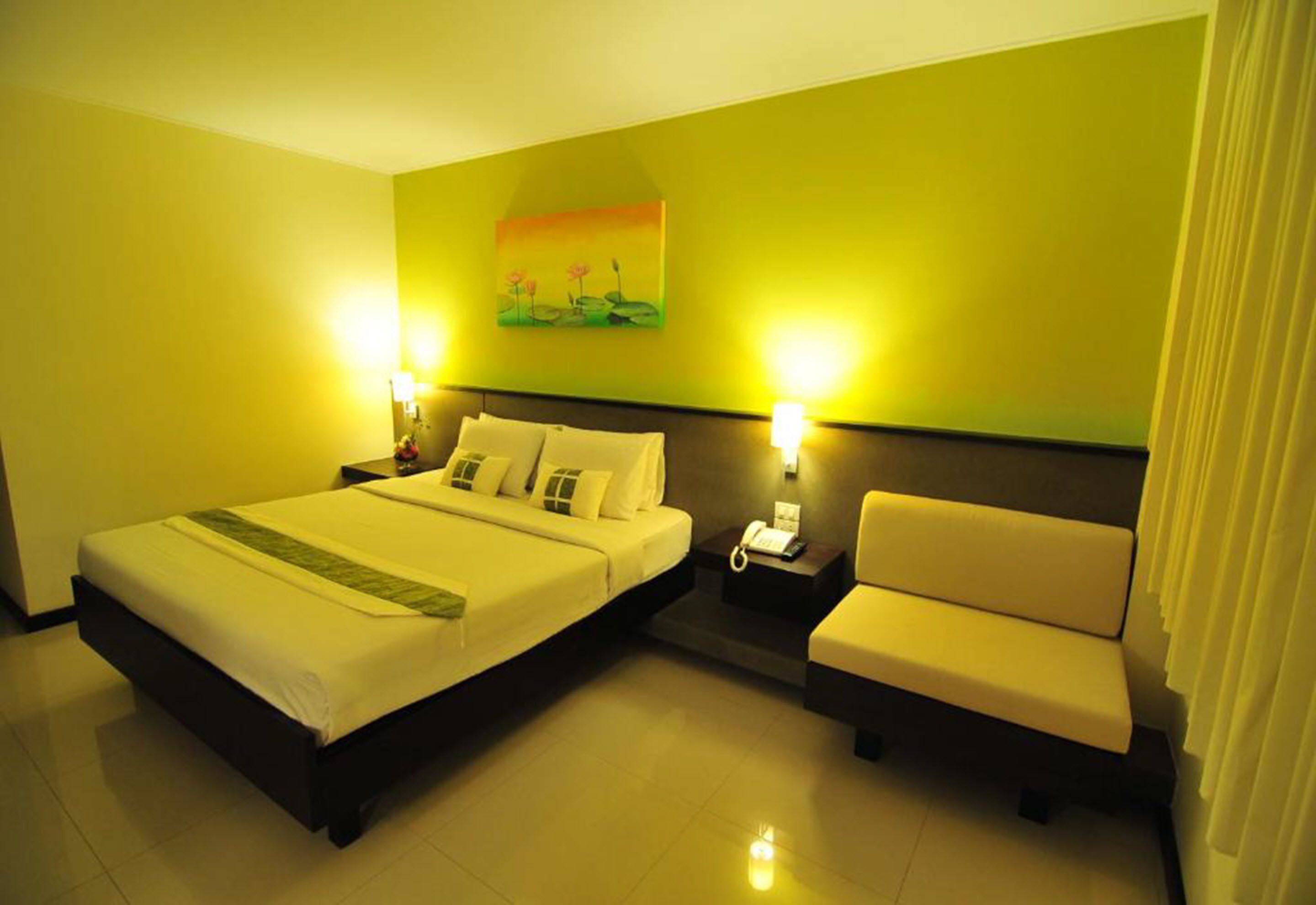 Habitación de hotel con una cama grande, una mesita de noche con lámpara, una silla y un cuadro en la pared.