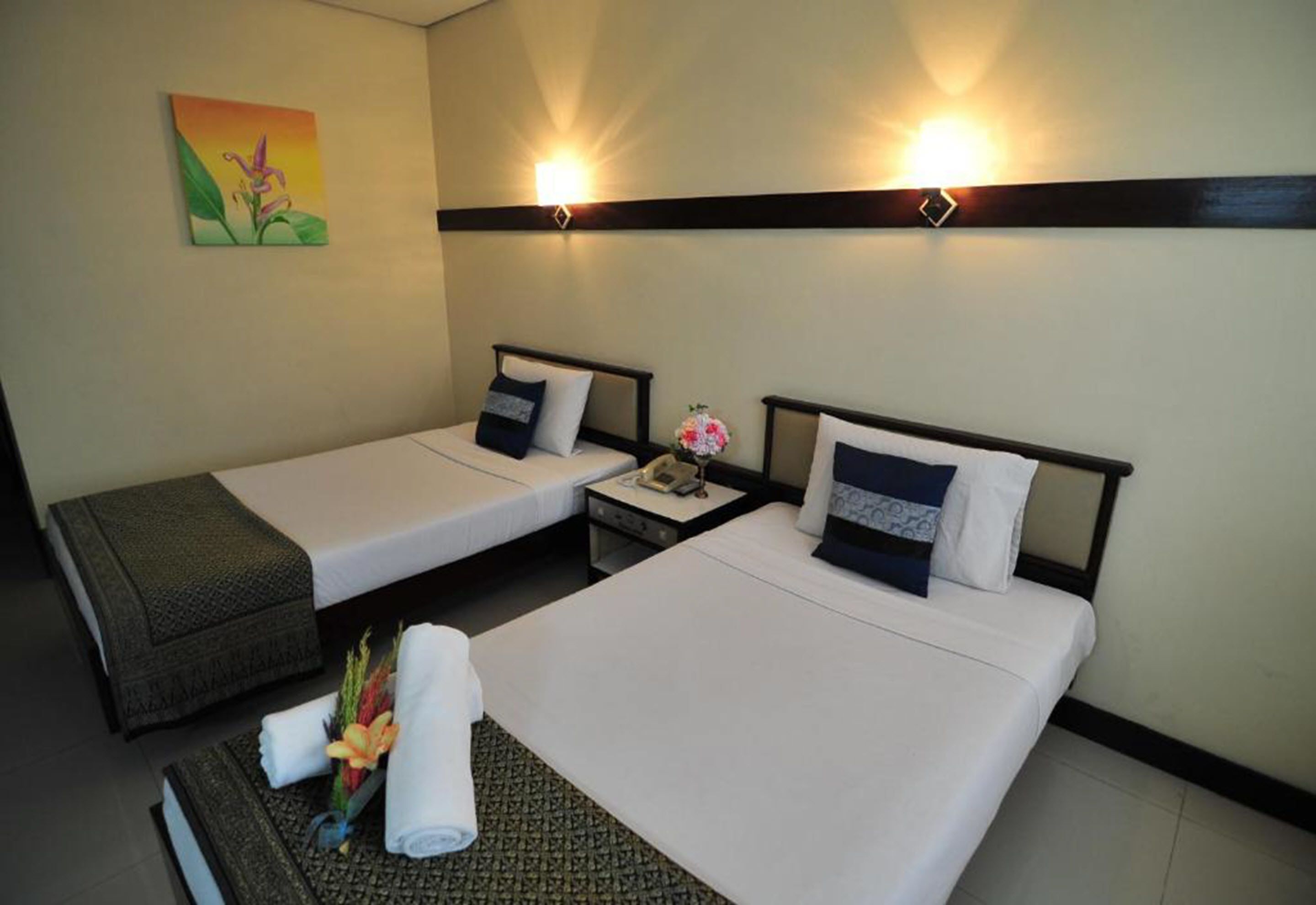 A hotel room with two single beds, a small table with a phone, and a painting on the wall.