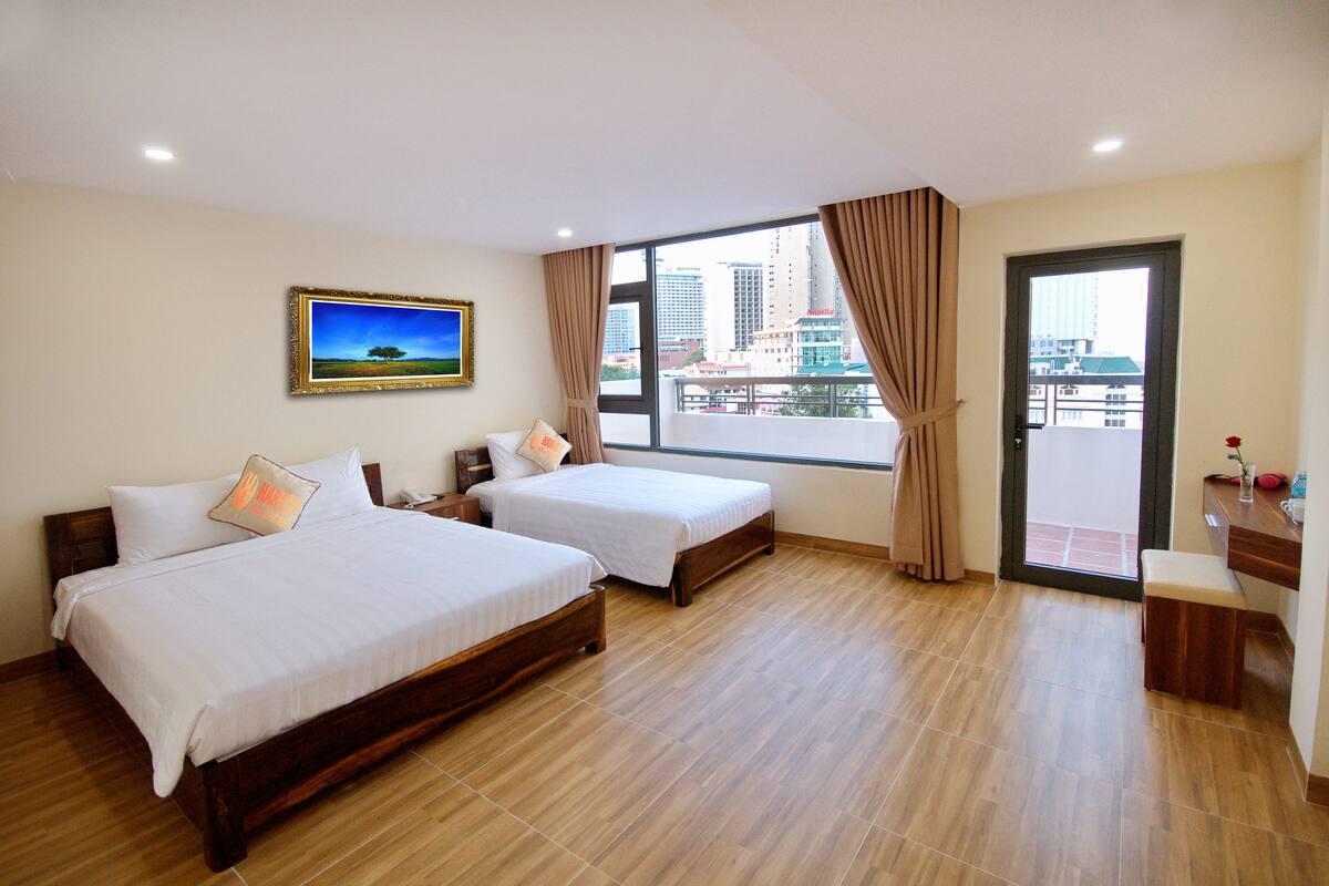 A hotel room with two beds, a large window with curtains, a wooden floor, and a city view.