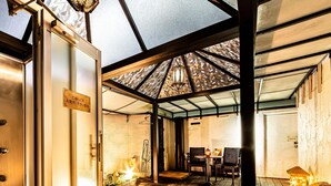 A hotel entrance with a glass door, a sign, a seating area with tables and chairs, and a decorative lantern.