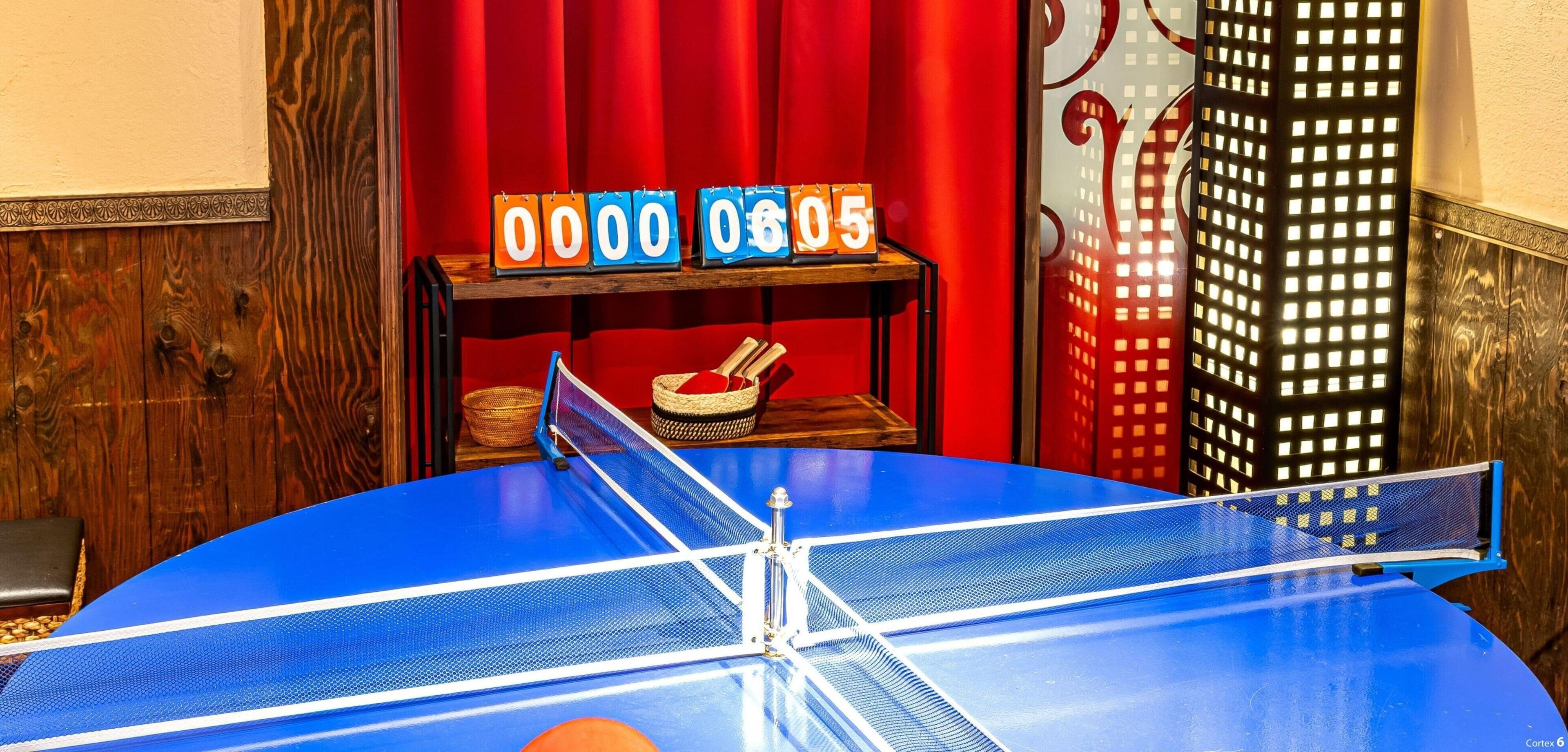 Ein Pingpongtisch mit rotem Vorhang im Hintergrund und einer Uhr, die 06:05 anzeigt.