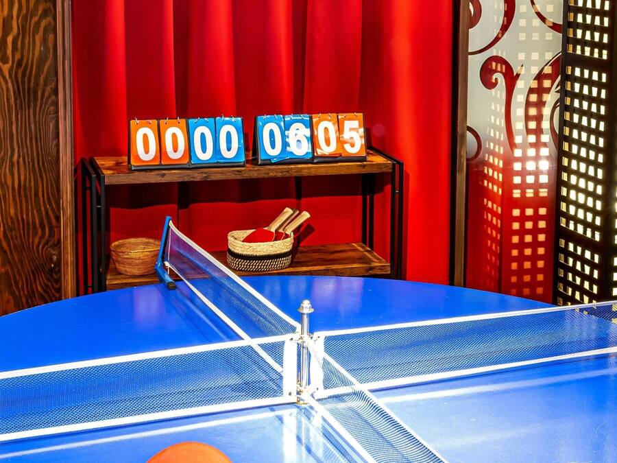 Ein Pingpongtisch mit rotem Vorhang im Hintergrund und einer Uhr, die 06:05 anzeigt.
