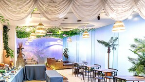 An indoor space with a dining area, tables, chairs, and a wall with a large screen displaying a nature scene.