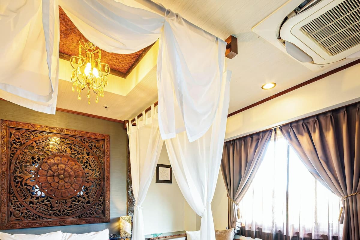 A room with a canopy bed, a chandelier, a large decorative panel, and a ceiling air vent.