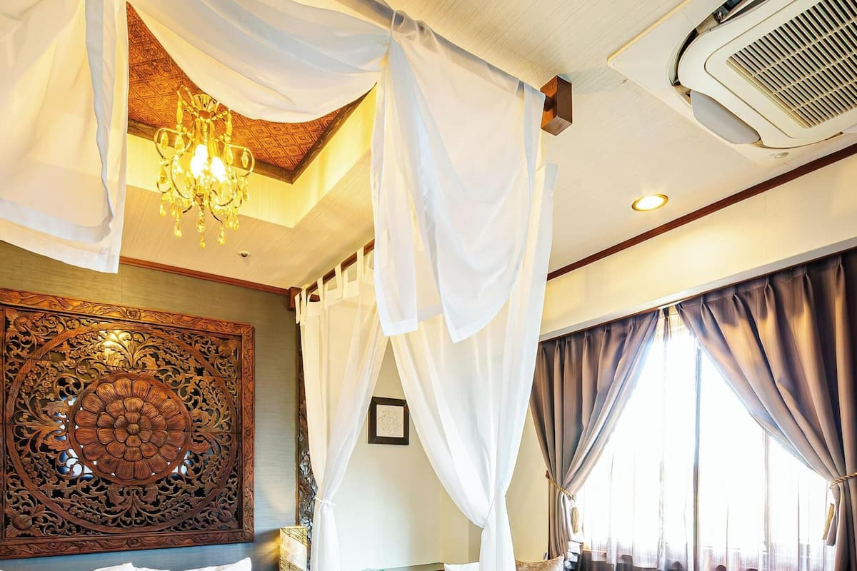 A room with a chandelier, a large decorative panel, and a bed with curtains.