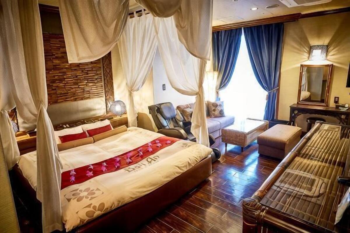 A four-poster bed with a canopy, a sitting area with a sofa and armchairs, and a piano.