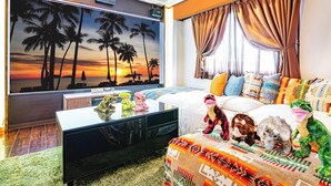 A hotel room with a large TV, a bed with patterned bedding, a plush rug, and a window with curtains.