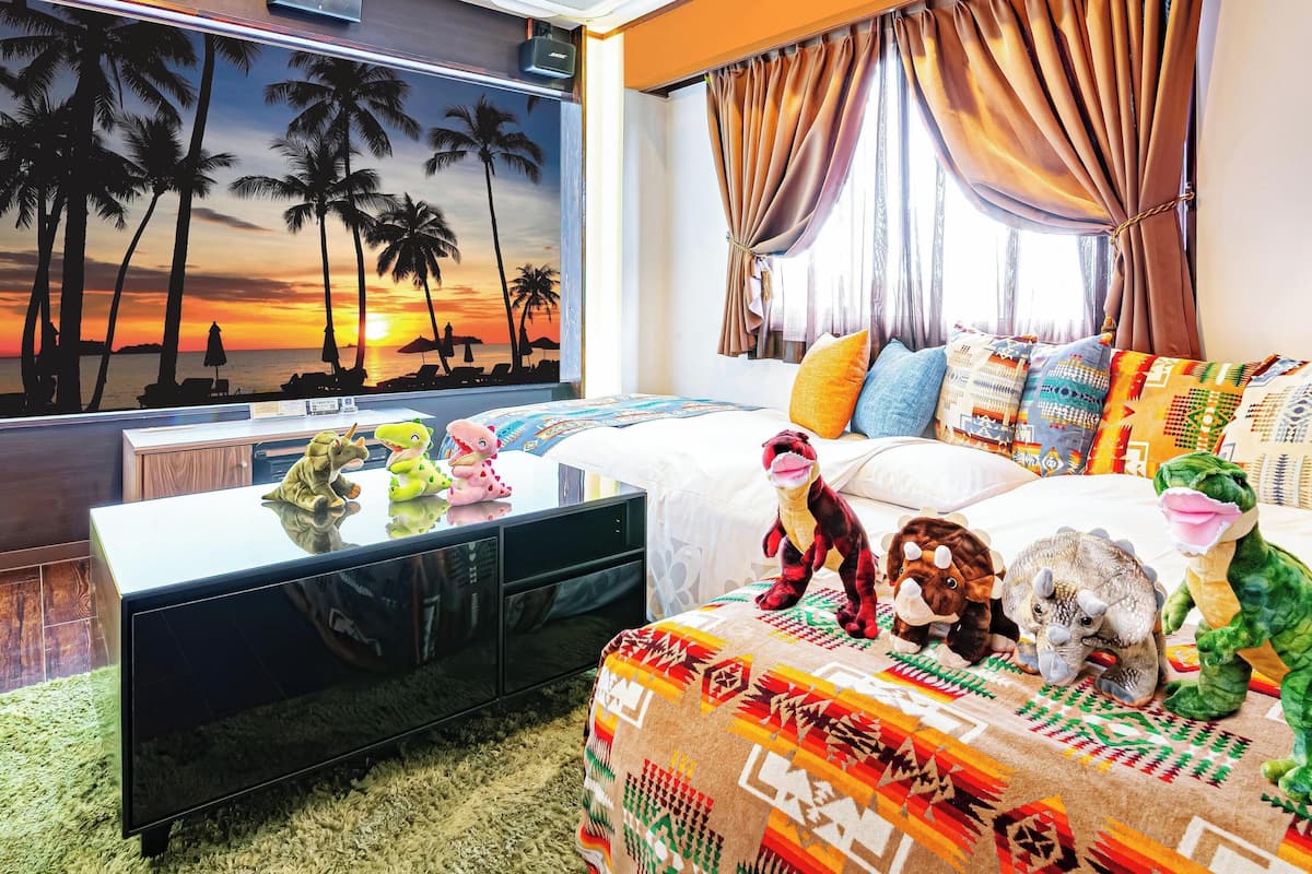 A hotel room with a large TV, a bed with patterned bedding, a plush rug, and a window with curtains.