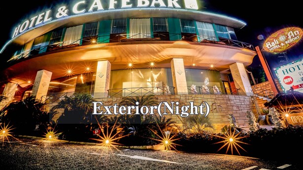A hotel exterior at night with illuminated signage, a balcony, and a parking sign.