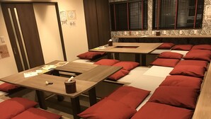 A hotel room with multiple beds, each with red pillows and a wooden table. There are signs on the wall and a window with blinds. - Guest House One More Heart at NARA DEN - Hostel (Nara)