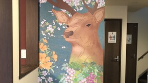 A hallway with a mural of a deer surrounded by flowers. There is a door labeled "Shower Room" and another door labeled "Restroom." - Guest House One More Heart at NARA DEN - Hostel (Nara)