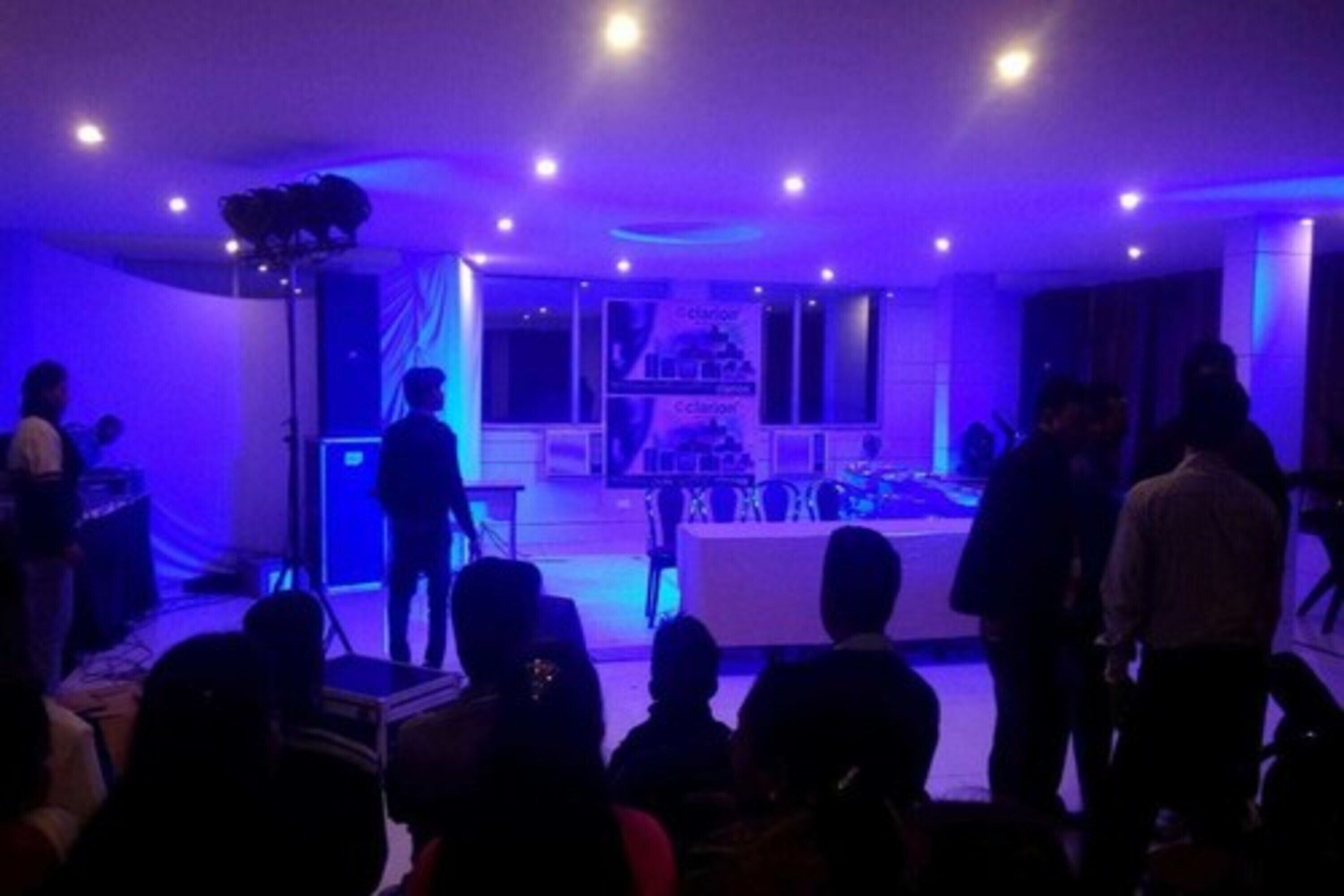 An indoor event space with a stage, audience seating, and a DJ booth.