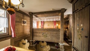 Una habitación rústica con paredes de madera, un banco de madera, una mesita con un jarrón y una ventana con cortina a cuadros.