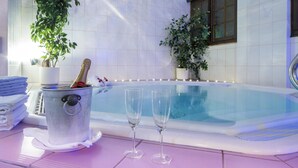 Zona de spa con bañera de hidromasaje, una botella de champán y copas sobre piso de baldosas.