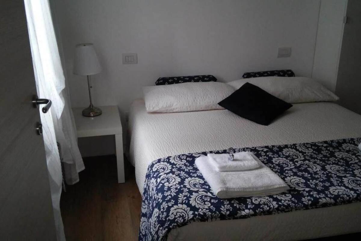 Et hotelværelse med seng, natbord, lampe og dør.