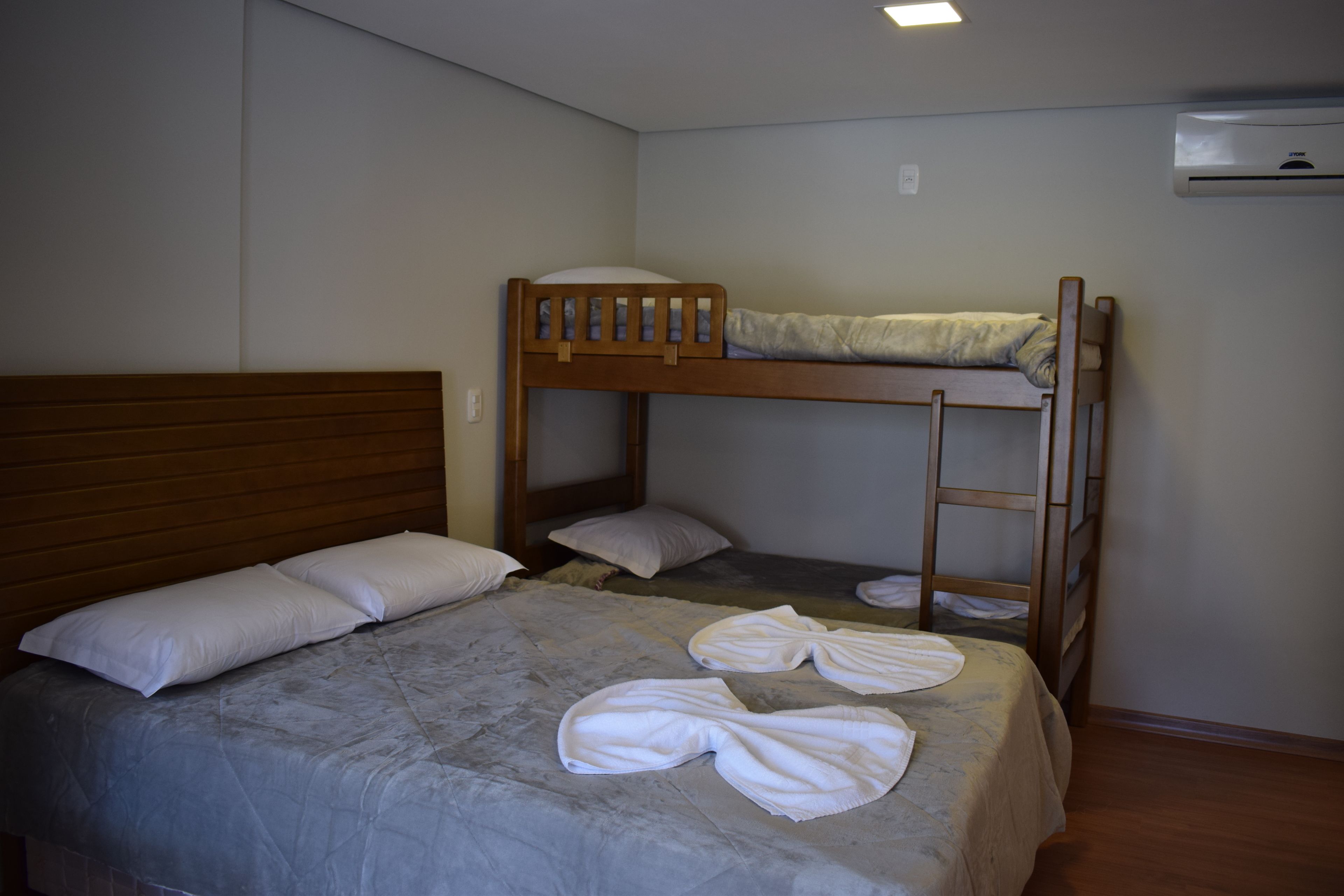 A bunk bed room with a wooden headboard, a single bed with a quilt, and two white towels on the bed.
