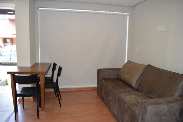 A room with a wooden dining table, black chairs, and a brown sofa.