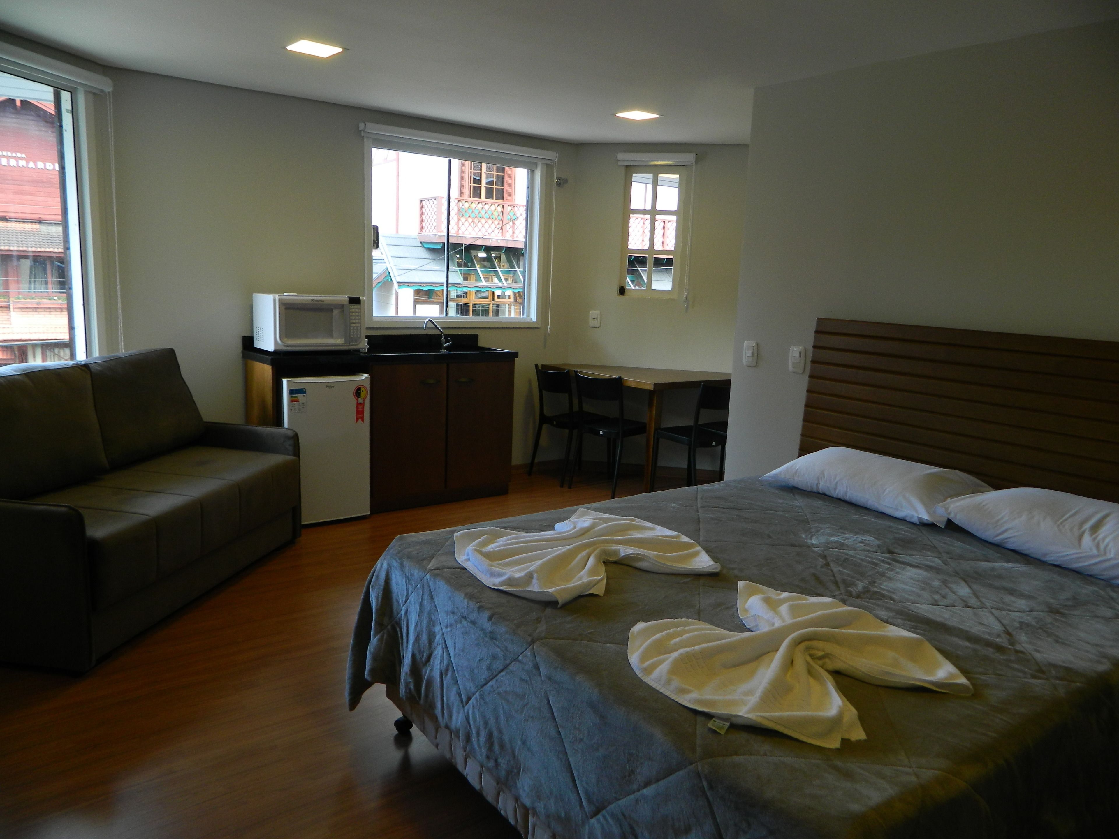 A compact hotel room with a bed, a small kitchenette, a sofa, and a desk.